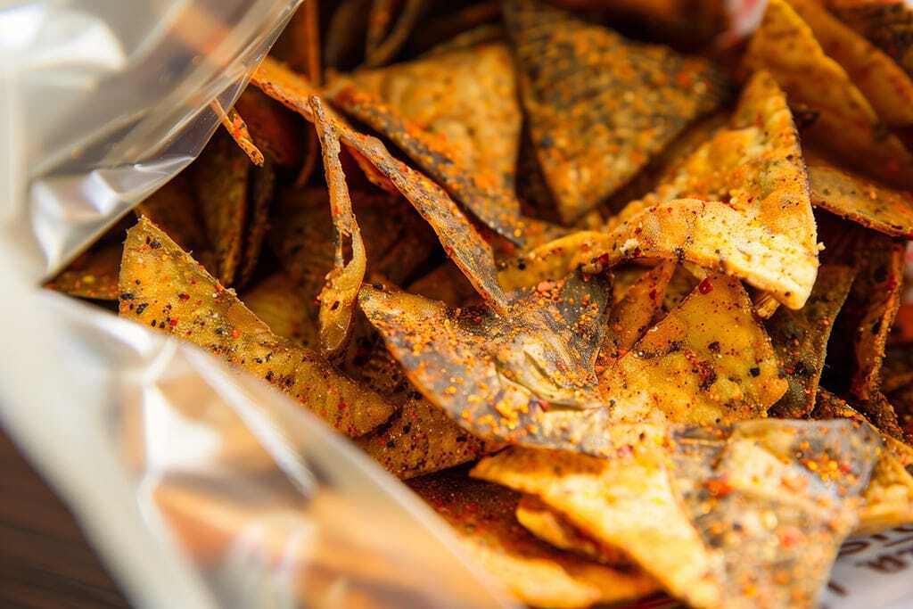 Close-up of a bag of seasoned tortilla chips with visible spices and vibrant colors, highlighting their crispy texture and flavor. San Diego healthy vending service and office coffee solutions